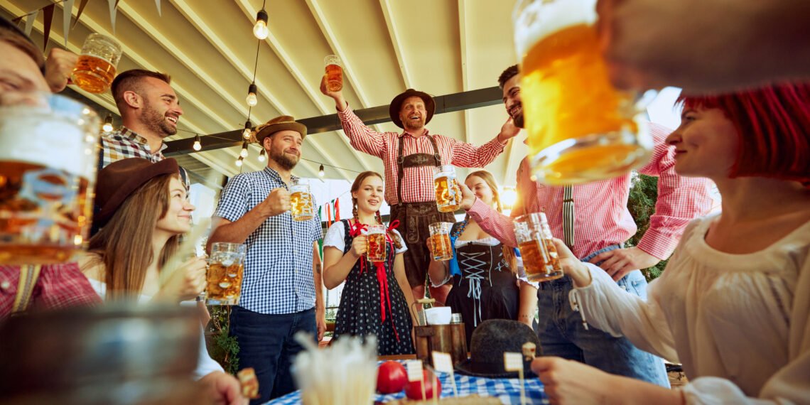 Men in traditional Bavarian clothes cheering group of his friends, people meeting at local pub for beer festival celebration. Concept of Oktoberfest, festival, party, brewery, traditions